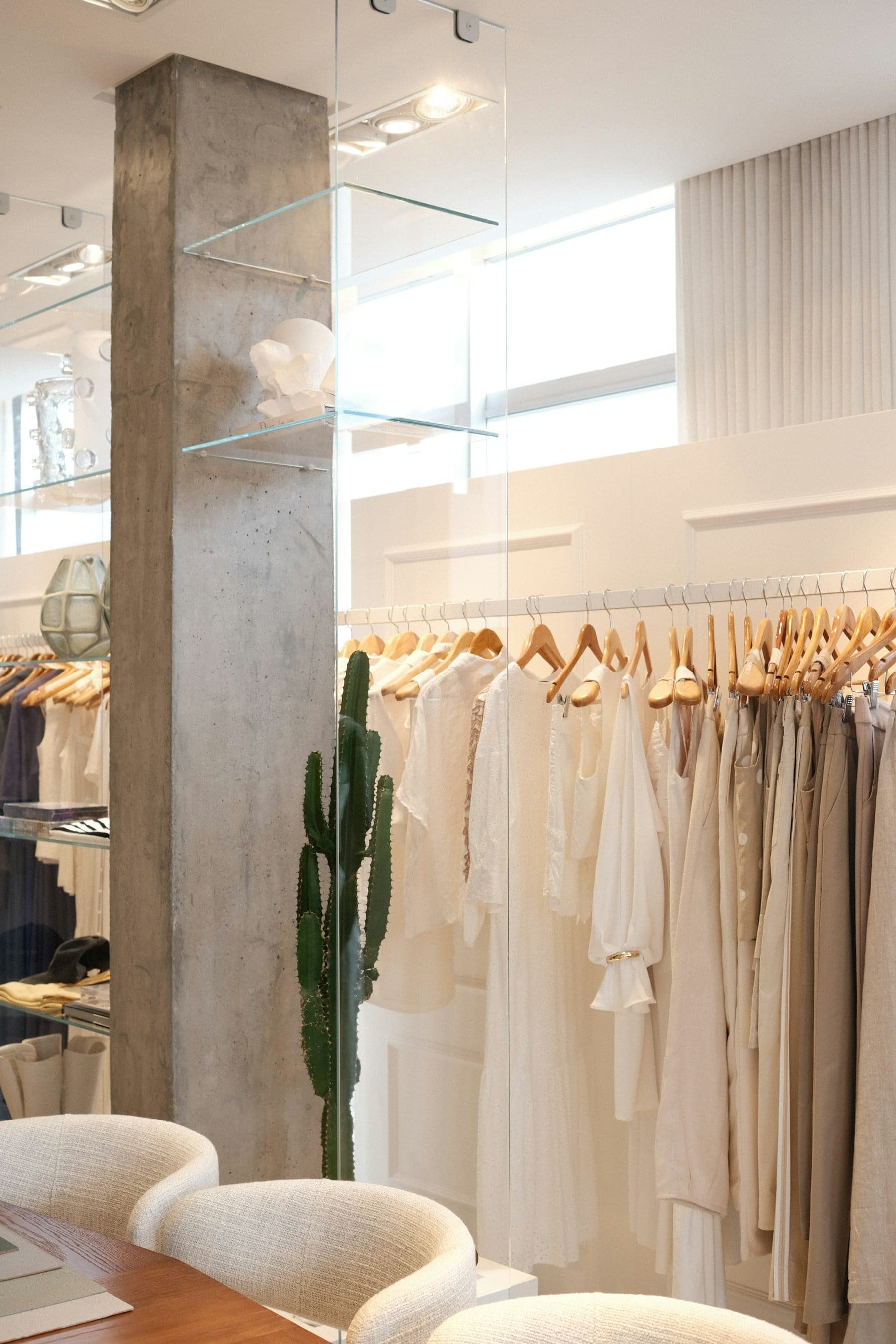 A calm, minimal boutique interior with neutral garments and a plaster-finished column