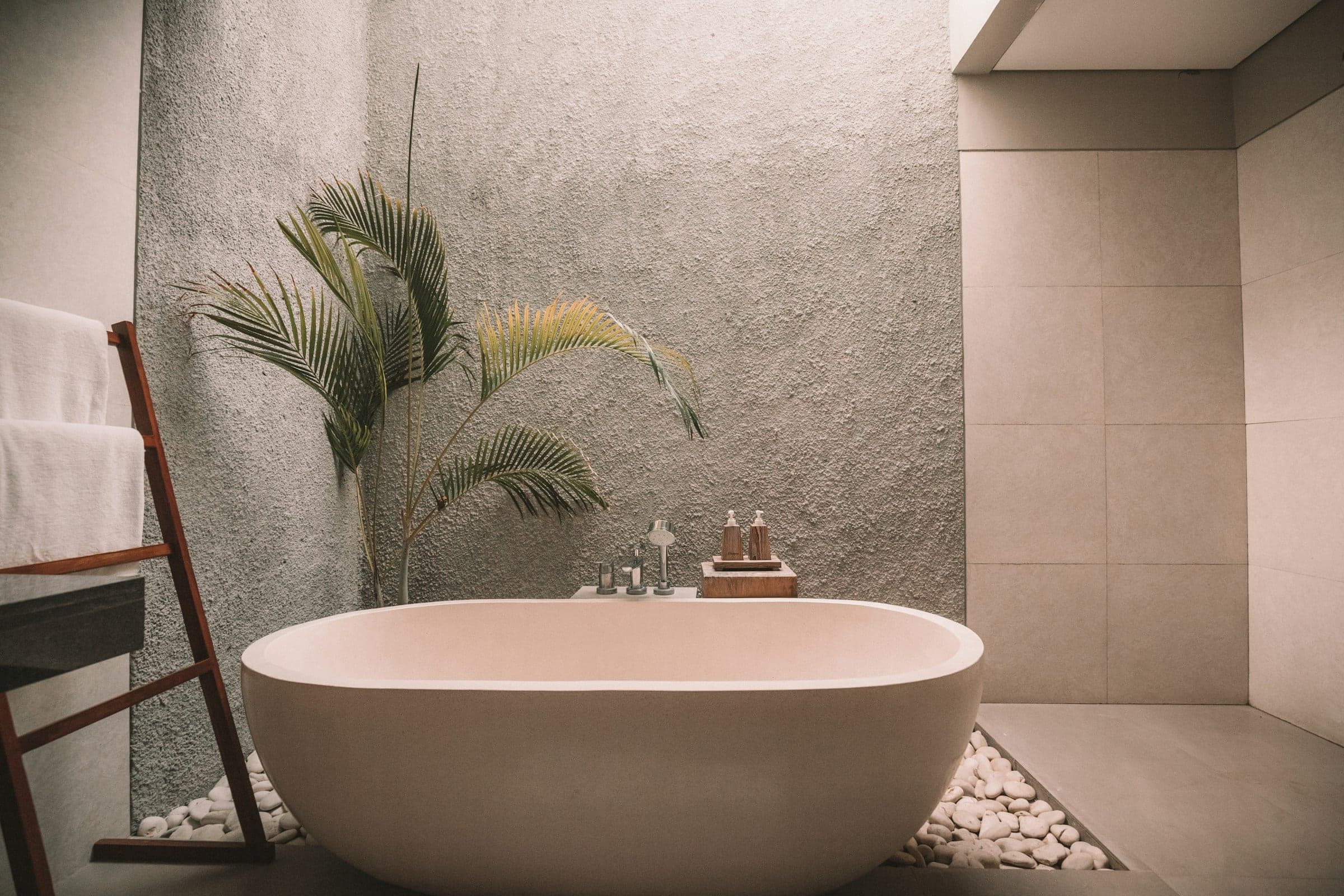 A freestanding bath before a textured, stone-toned plaster wall